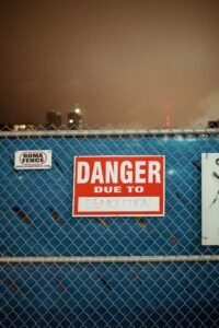 Red danger sign on chain link fence warning of demolition on city construction site.
