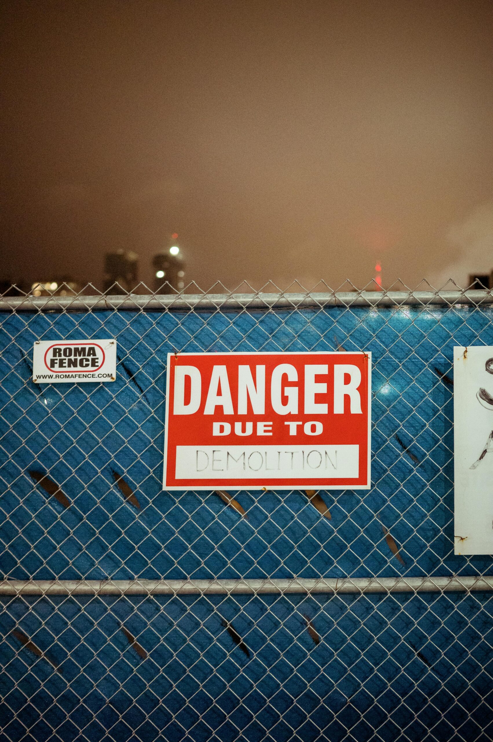 Red danger sign on chain link fence warning of demolition on city construction site.